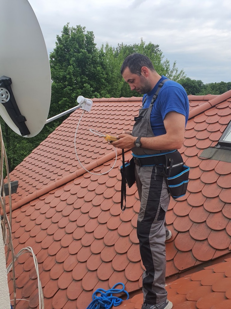 Instalator na dachu reguluje antenę satelitarną.