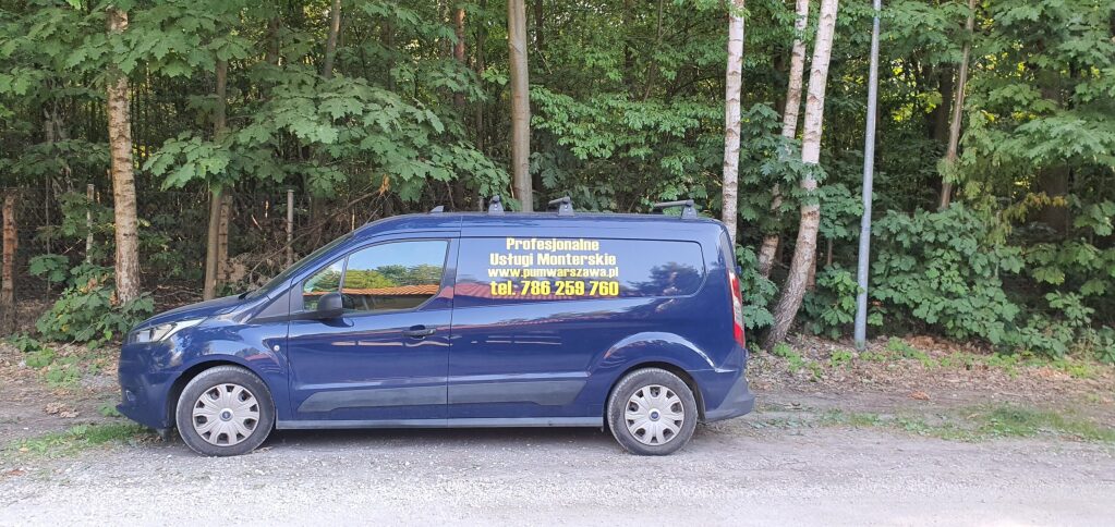 Granatowy van firmy "Profesjonalne Usługi Monterskie" z numerem telefonu 786 258 760 zaparkowany na tle zielonego lasu.