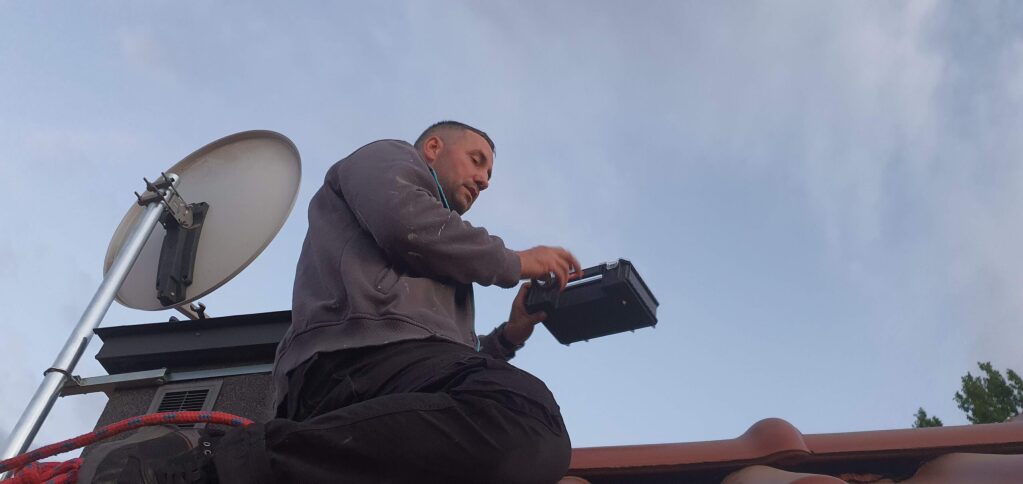 Fachowiec wykonuje montaż anteny satelitarnej na dachu, korzystając z przyrząd&oacute;w pomiarowych. Usługi IT i montaż anten Pruszk&oacute;w.